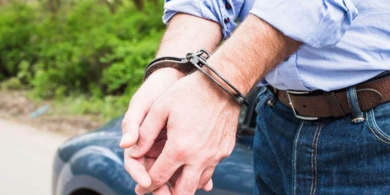 Man in blue shirt extends hand from blue car,