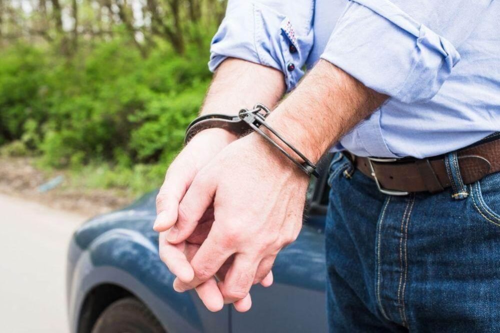 Man in blue shirt extends hand from blue car,