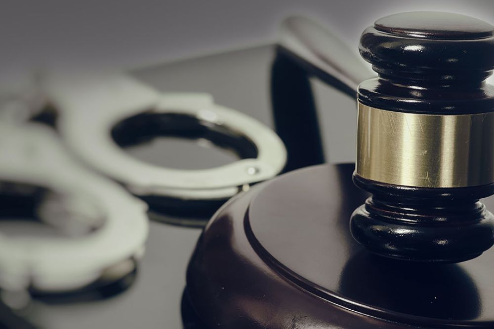 A wooden judge's gavel rests on its striking block, with handcuffs partially visible in the background, symbolizing law and justice.