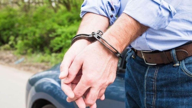 Man in blue shirt extends hand from blue car,