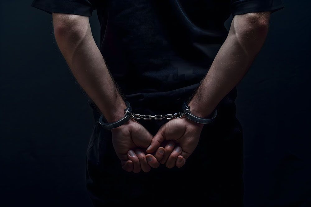 A person's hands are handcuffed behind their back against a dark background.