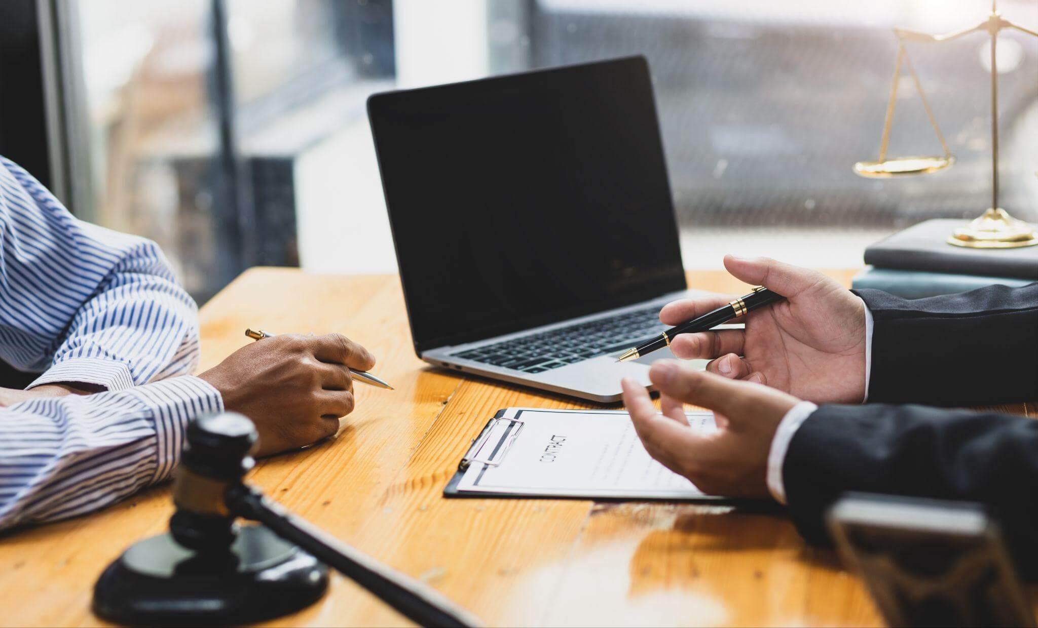 two people sitting at a table with a laptop and discussing an agreement
