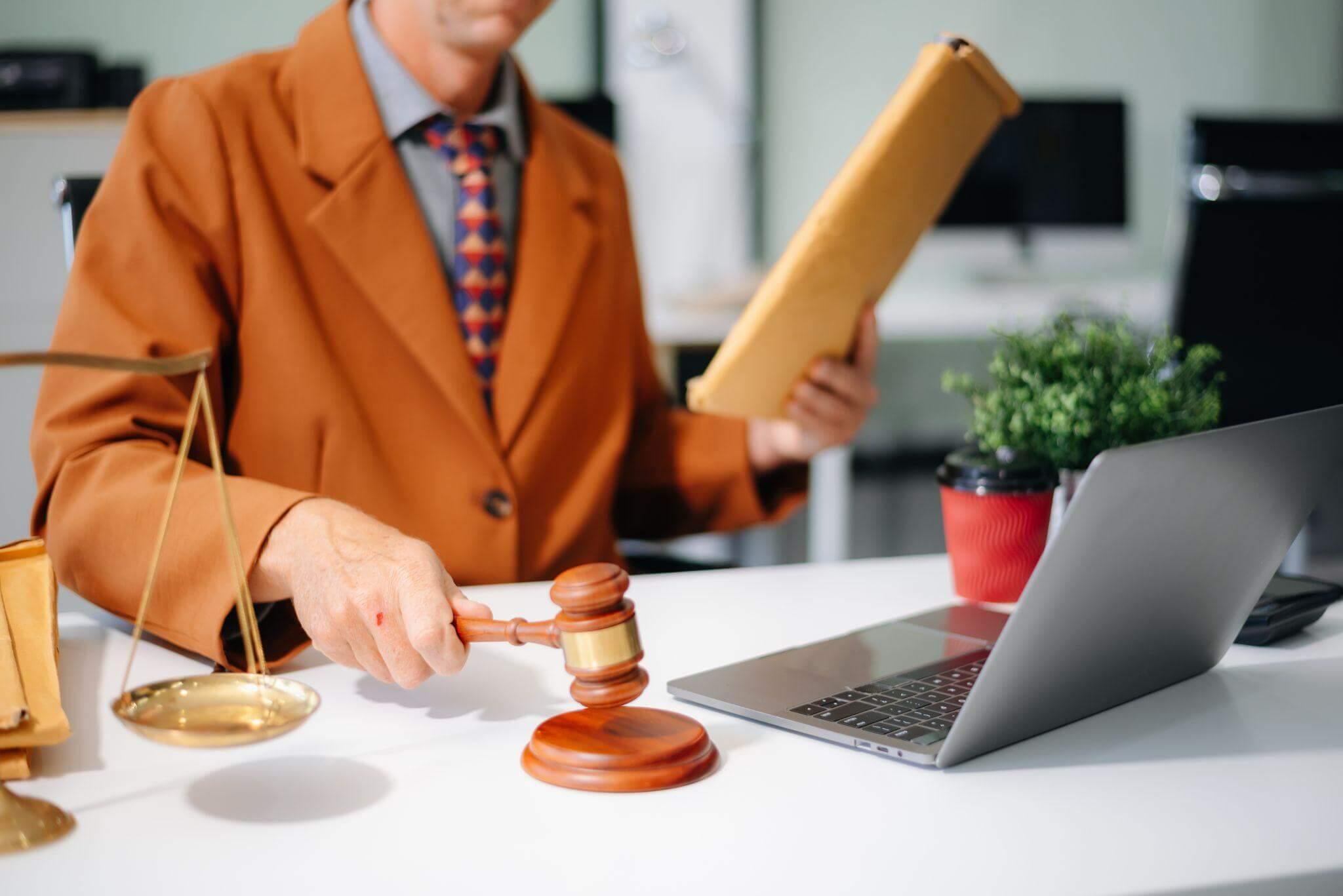 a man in a suit holding a gavel and a laptop as if dictating sentence
