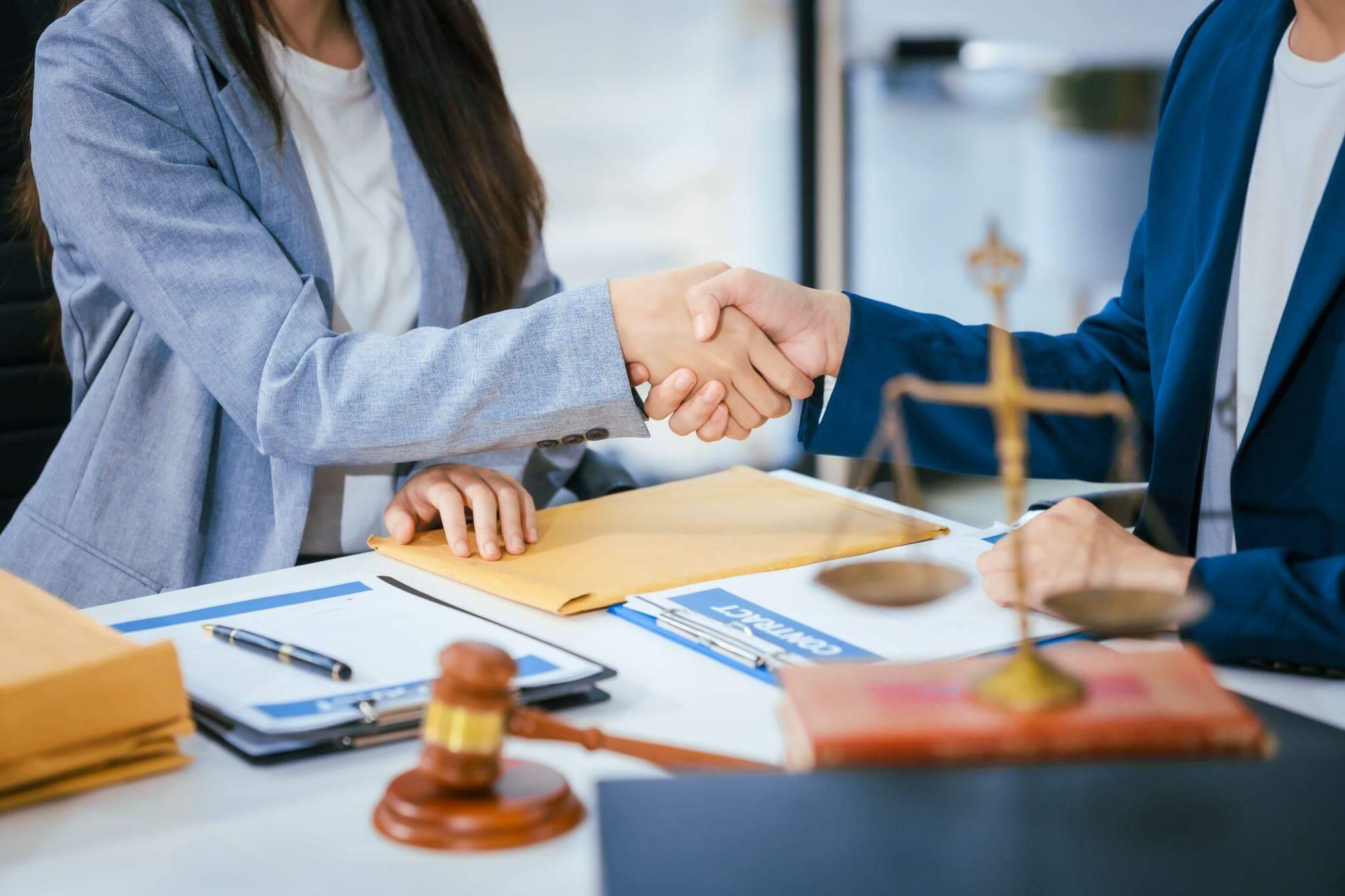 a couple of people shaking hands over a desk after reviewing legal documents
