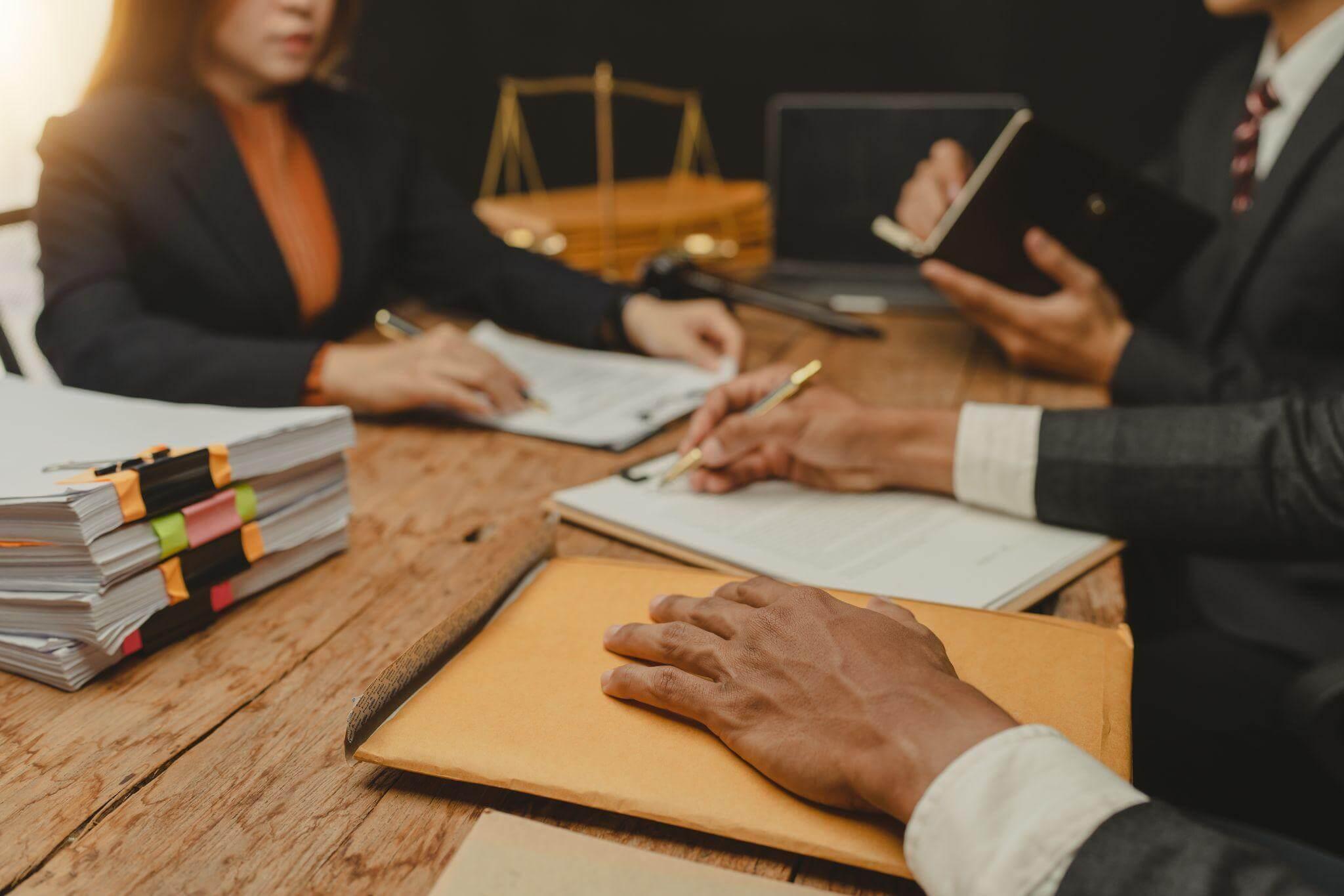 a group of people sitting around a wooden table reviewing legal documents