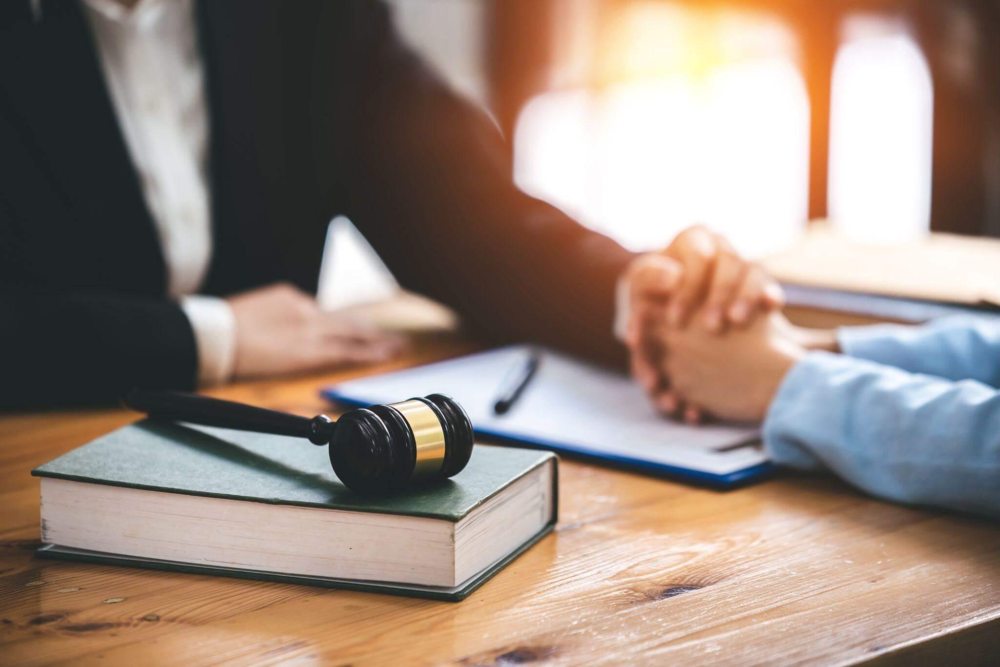 Two people shaking hands over an open book and a judge's gavel
