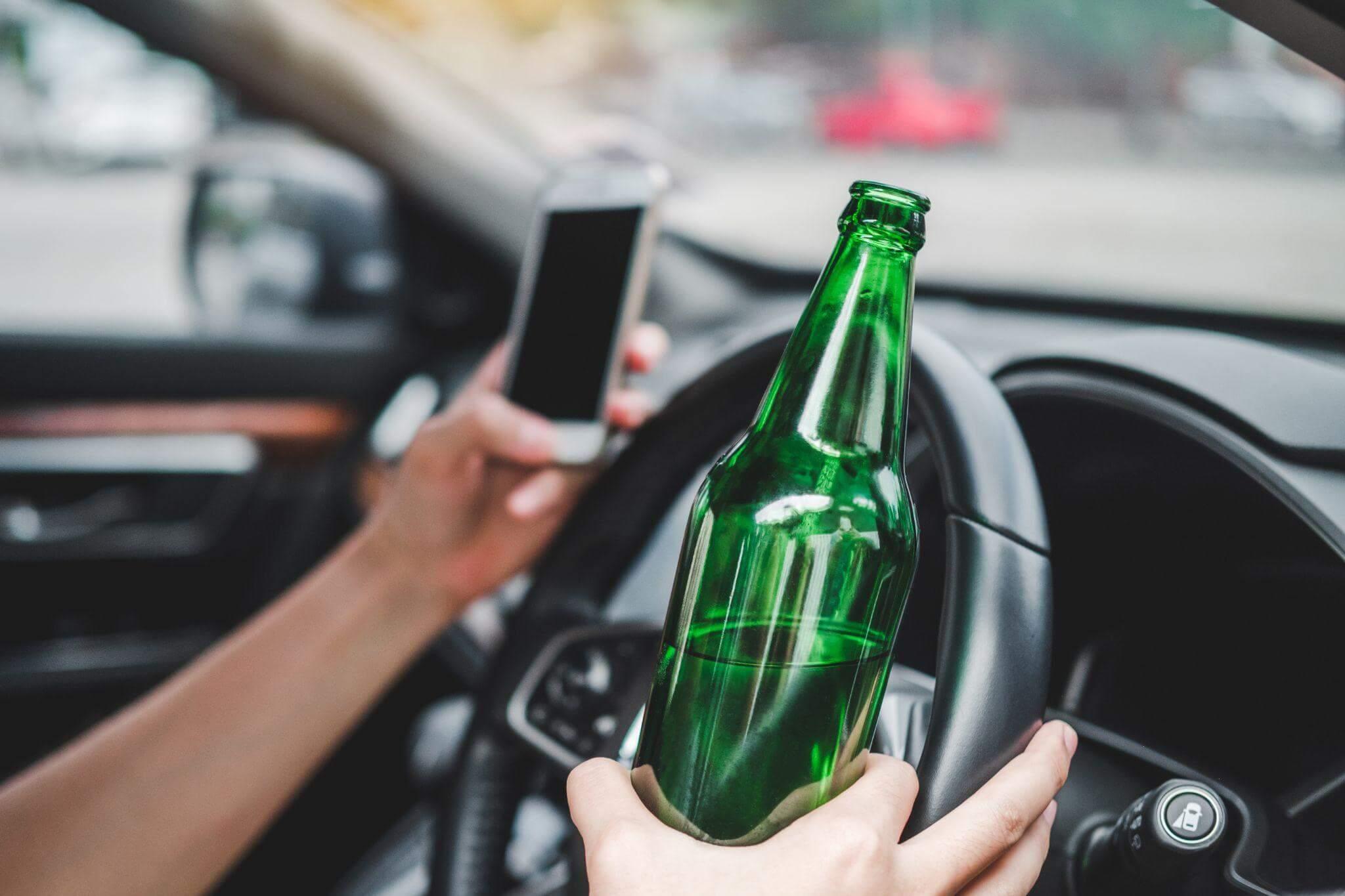 Person driving car with beer bottle, illustrating reckless behavior