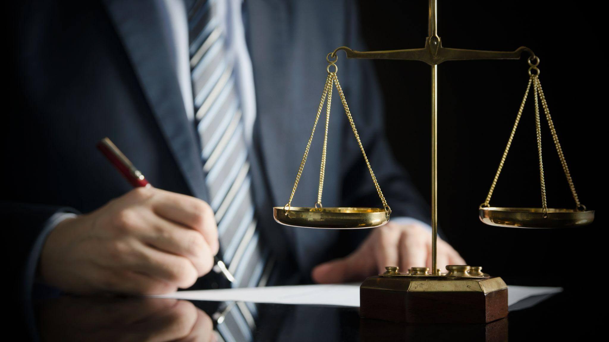Man in suit writing legal notes next to a scale